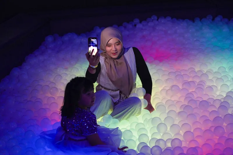 A mother photographing her daughter in the glowing LED ball pit at UFOREA Penang