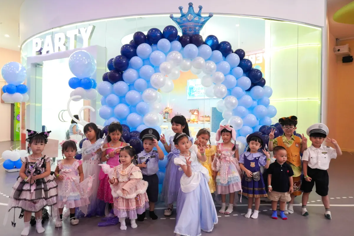 Costumed party guests in front of a blue balloon arch outside the UFOREA Penang party room