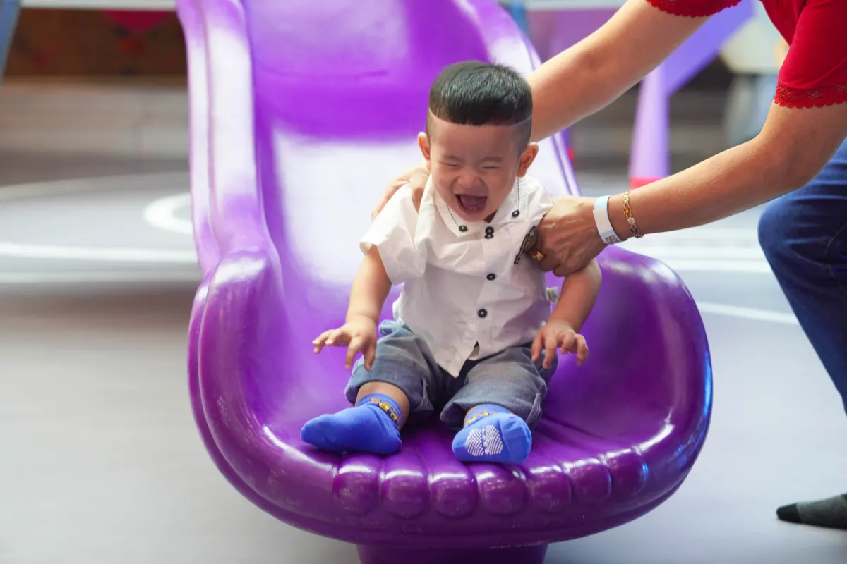 A laughing toddler coming down the purple slide at UFOREA Penang