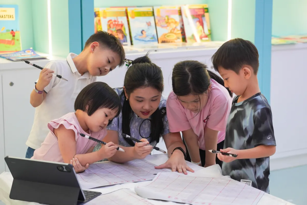 A UFOREA Penang host guiding children through a Chinese calligraphy workshop