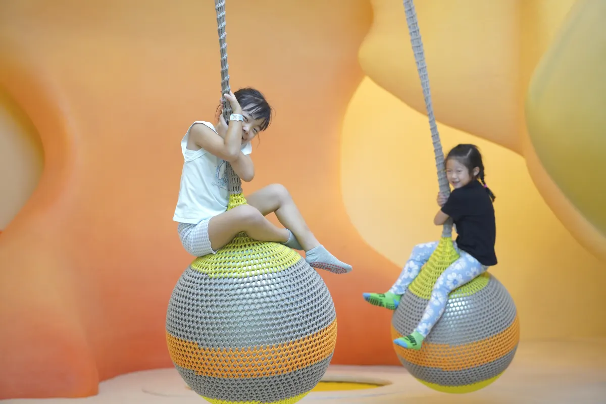 Two girls swinging on woven rope balls in the Discovery zone at UFOREA Penang
