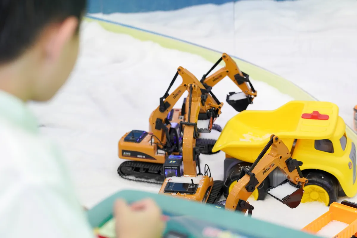 Remote-controlled orange excavators and a yellow tipper truck scoop white play sand in the Discovery Cove digger pit at UFOREA Penang