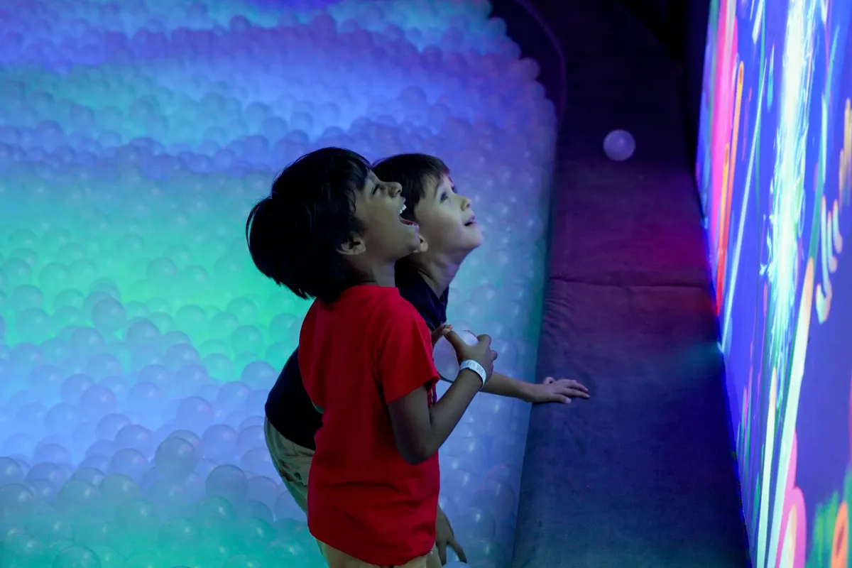 Two boys look up at the glowing interactive projection wall from the edge of the pastel-lit ball pit in the Dazzling Light Fantasy zone at UFOREA Penang