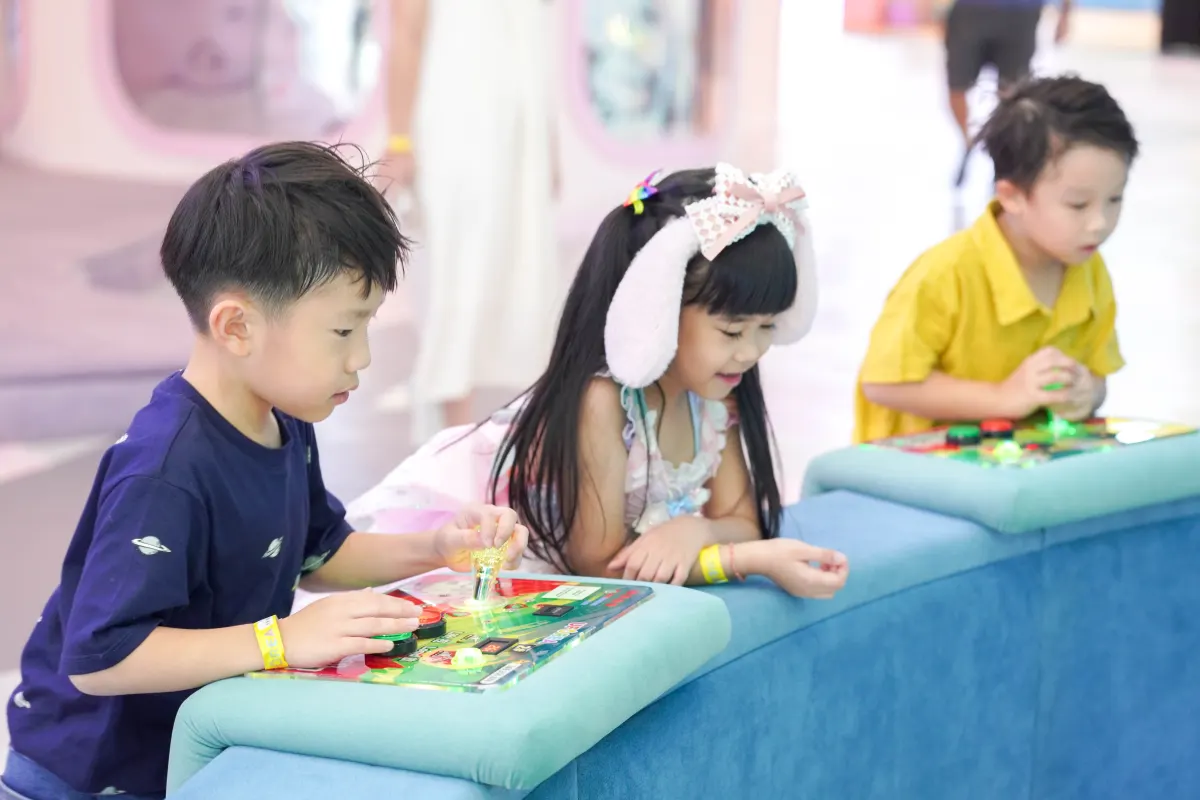 Three children lean over teal padded consoles playing the light-up tabletop arcade games at UFOREA Penang