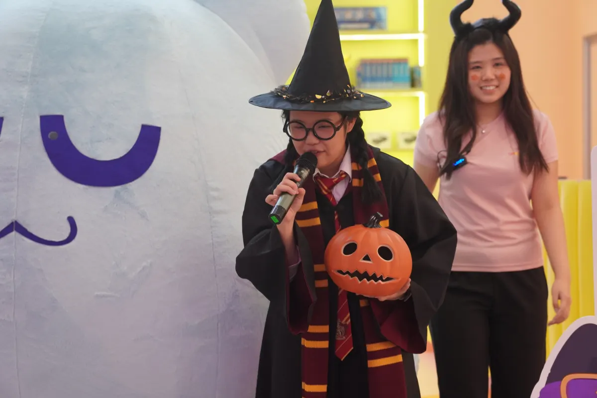 A costumed storyteller with a jack-o-lantern hosting the UFOREA Penang Halloween party