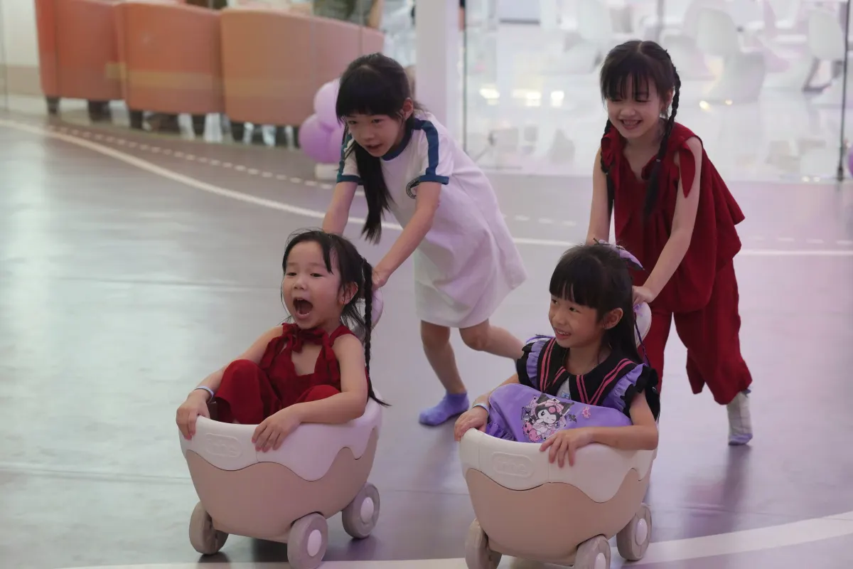 Four girls race one another in pastel push wagons along the painted road floor beside Mini Town at UFOREA Penang