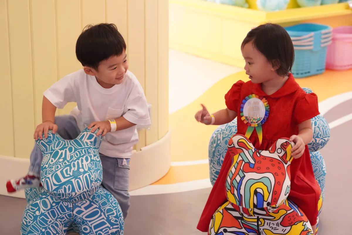 Two toddlers play together on brightly patterned ride-on animal toys in the toddler zone at UFOREA Penang, one pushing the other along