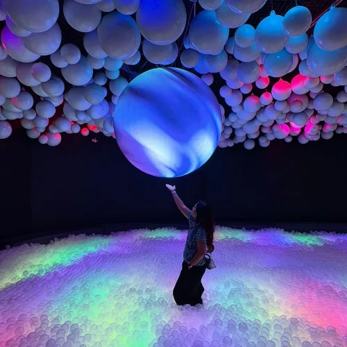 Fantasy Ball Pit N Led A visitor reaches up to touch a glowing illuminated sphere while standing in a vast rainbow-lit LED ball pit filled with thousands of softly lit balls in the Dazzling Light Fantasy zone at UFOREA Penang.