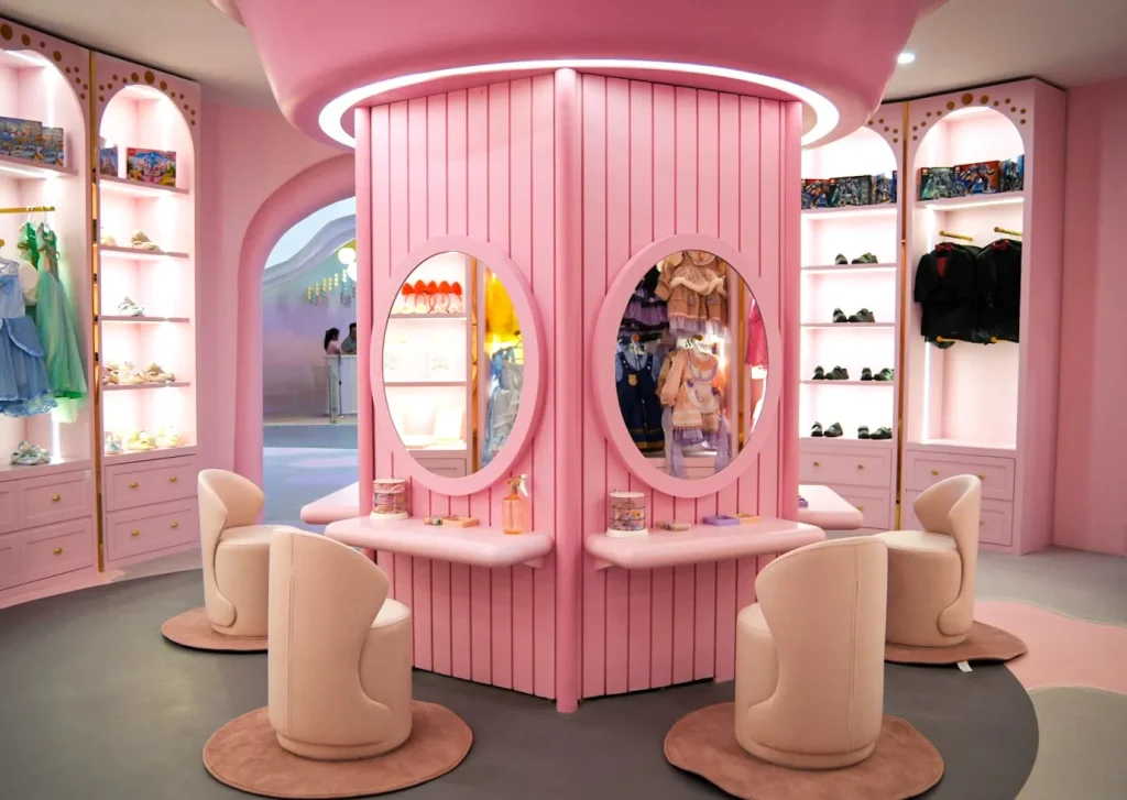 Inside the Makeover Castle salon at UFOREA Penang, a pink central vanity station with oval mirrors, plush cream swivel chairs on round rugs, and shelves displaying children's costumes and shoes.